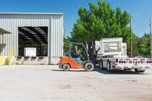 A team member operates a forklift to load a truck with newly manufactured ag system parts.
