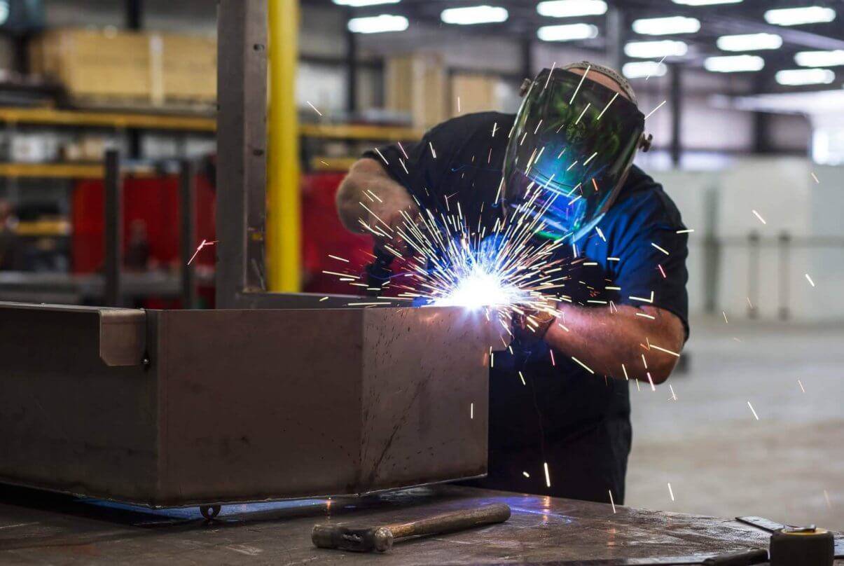 An employee wears a welding masks and sparks fly as he fuses sheets together.